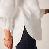 White button-up linen shirt with flared sleeves and ruffled trim.
