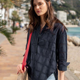 Woman standing on a coastal path holding a red bag, wearing a dark blue shirt and light blue jeans.