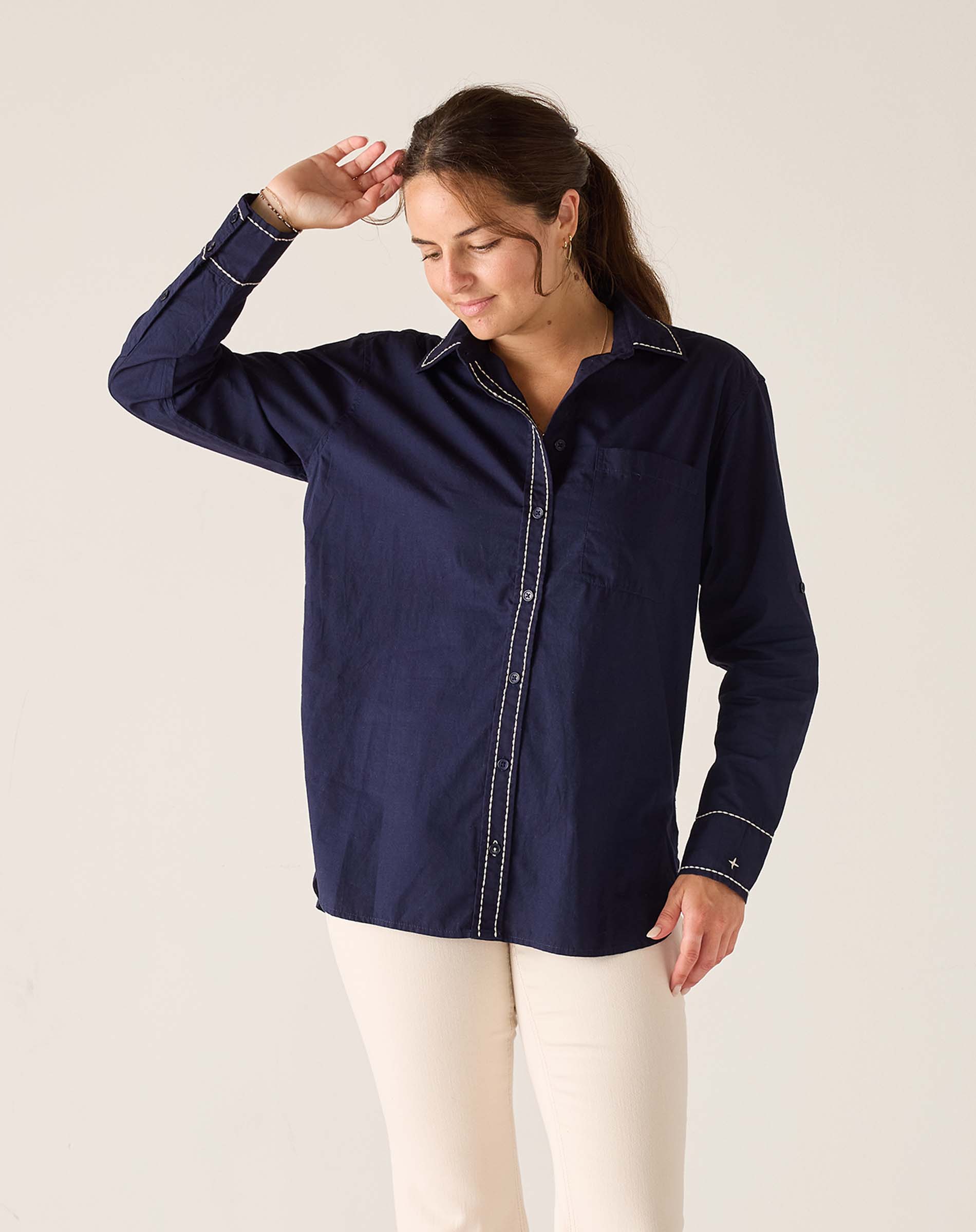 Woman wearing a navy blue shirt with white pants against a plain background