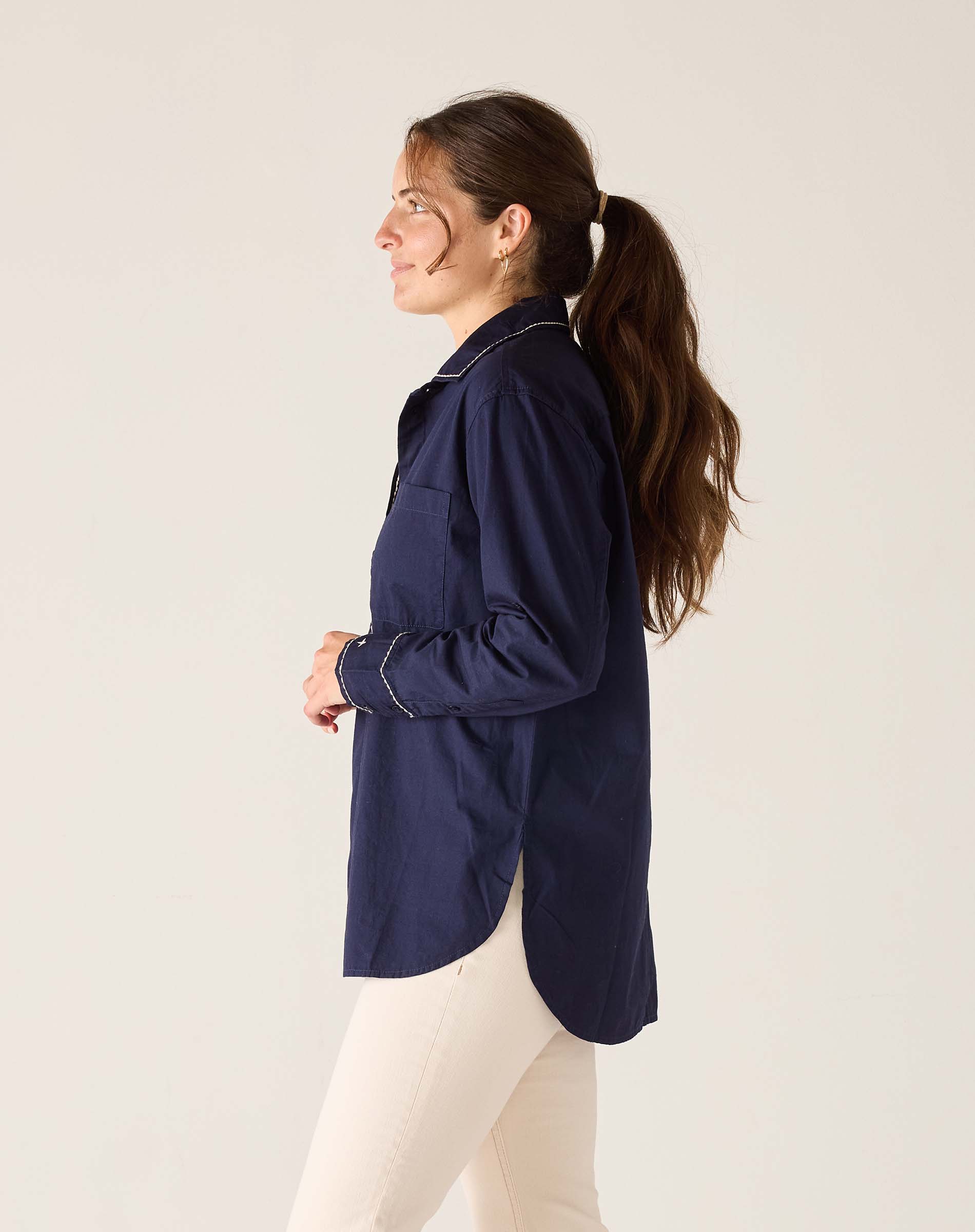 Woman wearing a navy blue shirt and white pants against a plain background