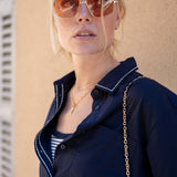 Woman wearing a navy blue jacket with a gold chain strap over her shoulder against a beige wall.