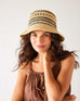 woman wearing calypso bucket hat with hand on neck in a brown dress