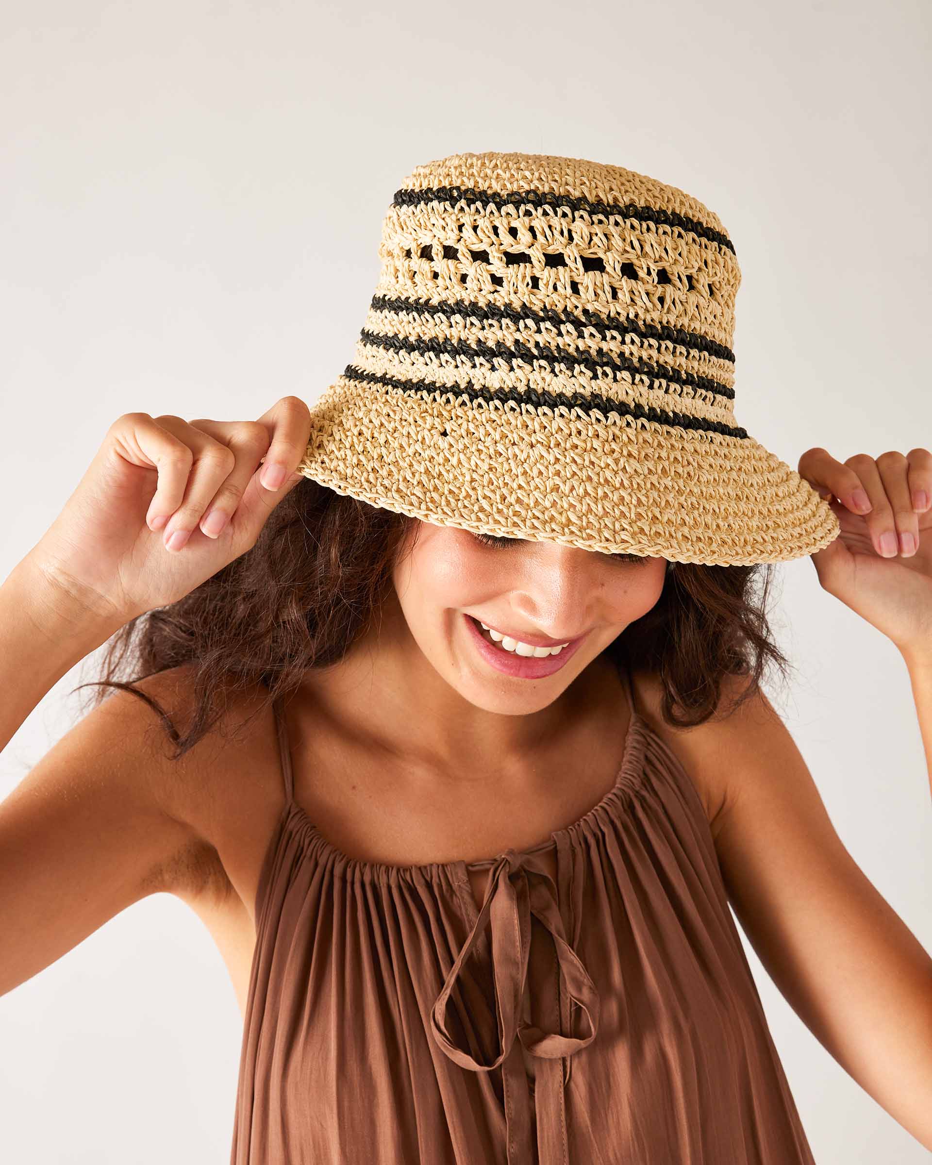 close up of woman wearing calypso bucket hat with hands on the brim of the hat
