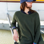 Person wearing a green sweater and cap, standing next to a small airplane.