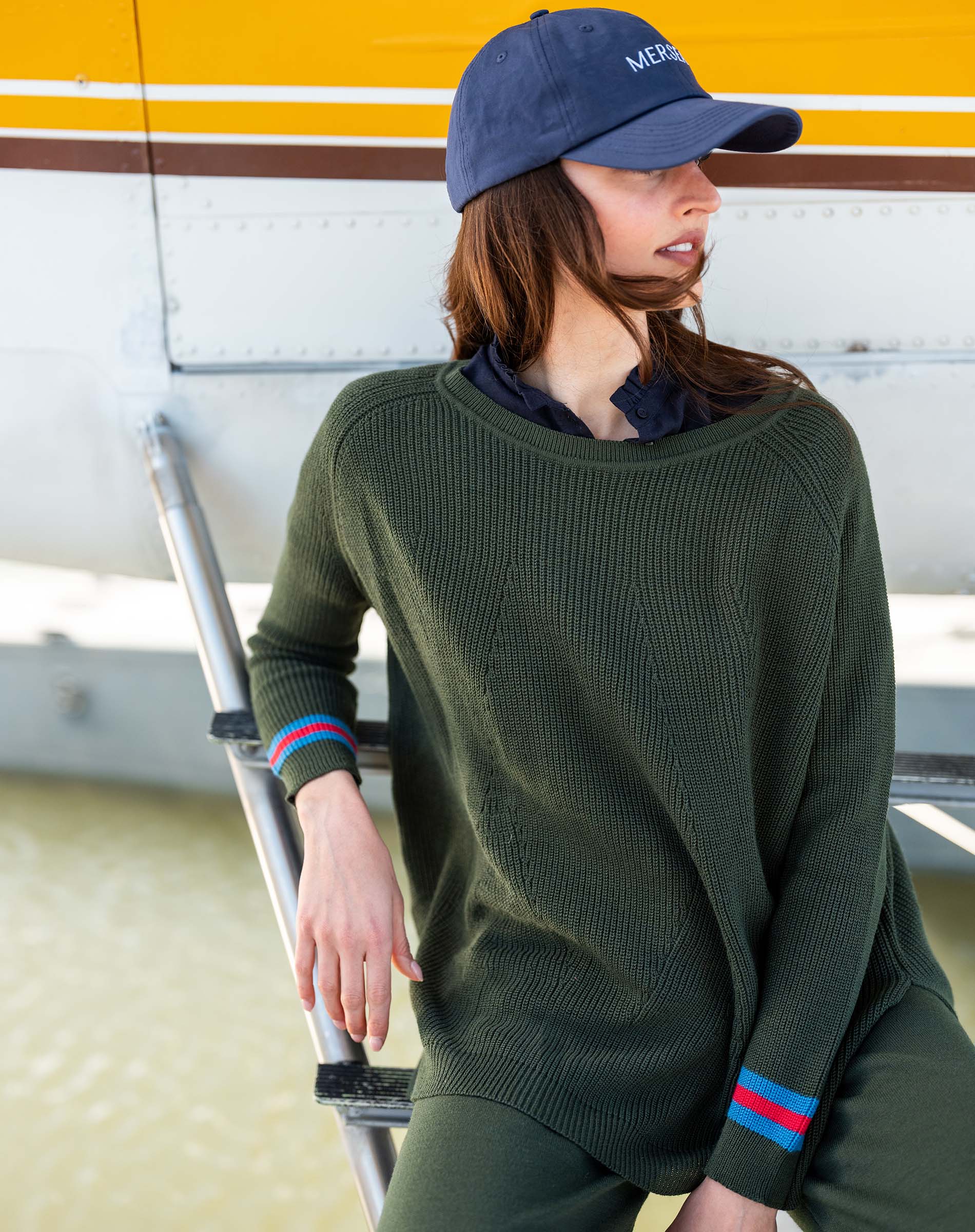 Person wearing a green sweater and cap, standing next to a small airplane.