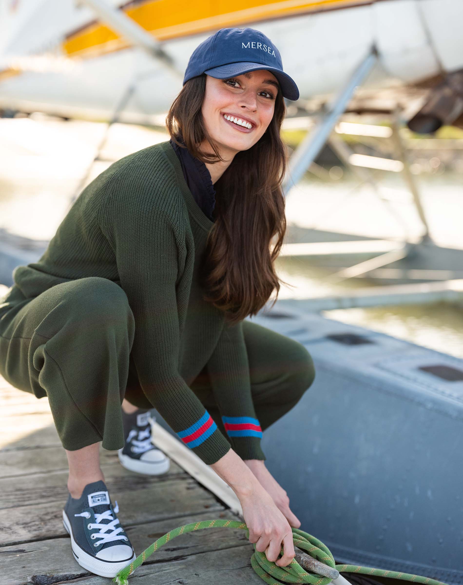 Woman tying a rope on a dock with a sailboat in the background