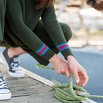 Person tying a green rope to a dock post on a wooden pier.