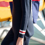Navy sweater with red and white stripe on sleeve worn by a person, blurred background