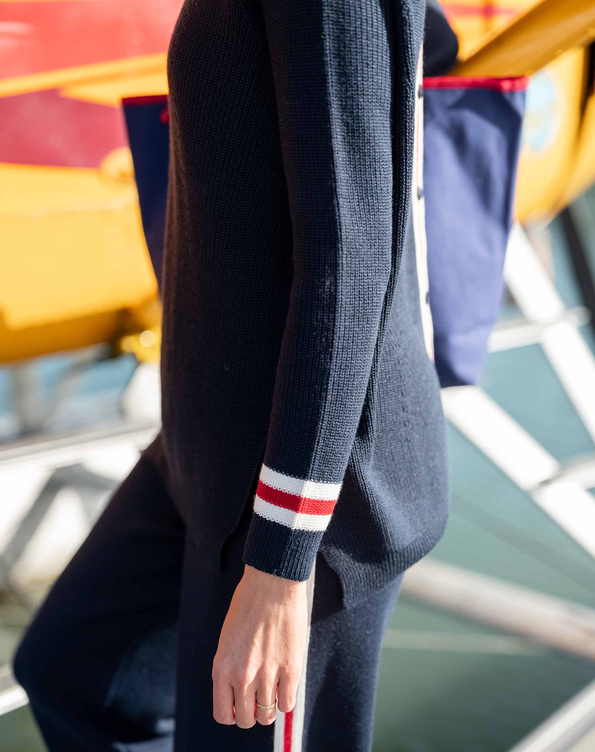 Navy sweater with red and white stripe on sleeve worn by a person, blurred background
