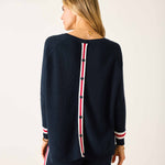 Woman wearing a navy sweater with red and white accents on a plain background
