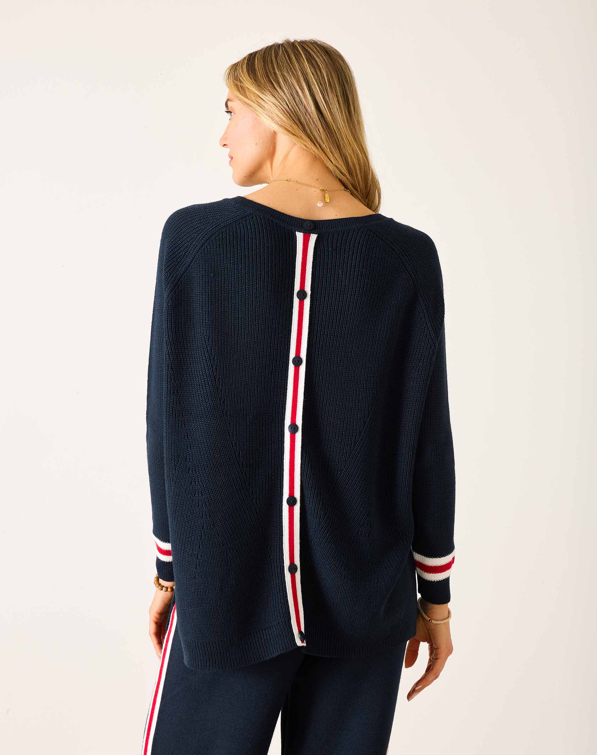 Woman wearing a navy sweater with red and white accents on a plain background