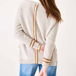 Person wearing a cream cardigan with brown accents and blue pants on a white background