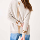 Person wearing a cream cardigan with brown accents and blue pants on a white background