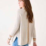 Woman wearing a cream cardigan with gold accents on a white background