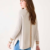 Woman wearing a cream cardigan with gold accents on a white background