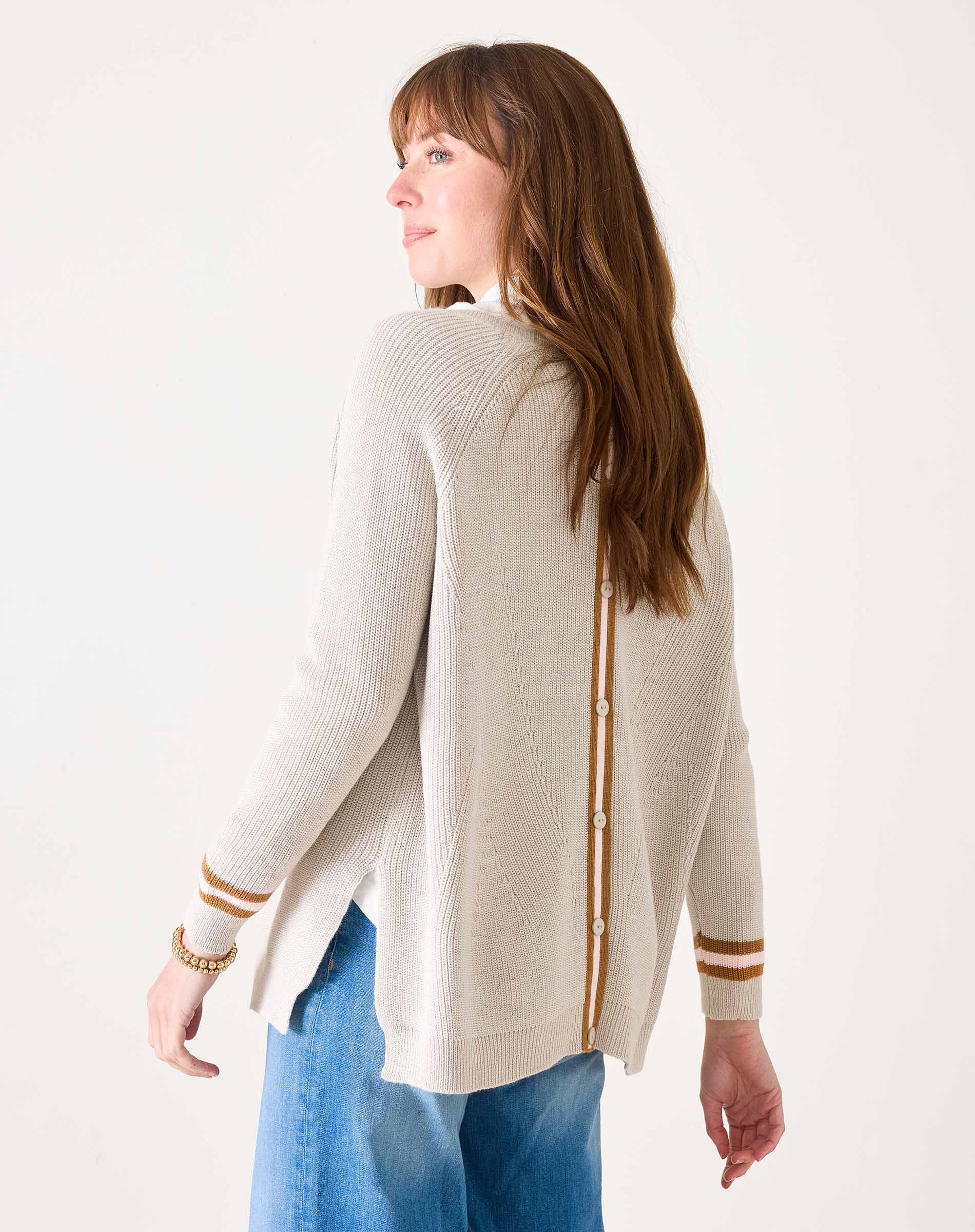 Woman wearing a cream cardigan with gold accents on a white background