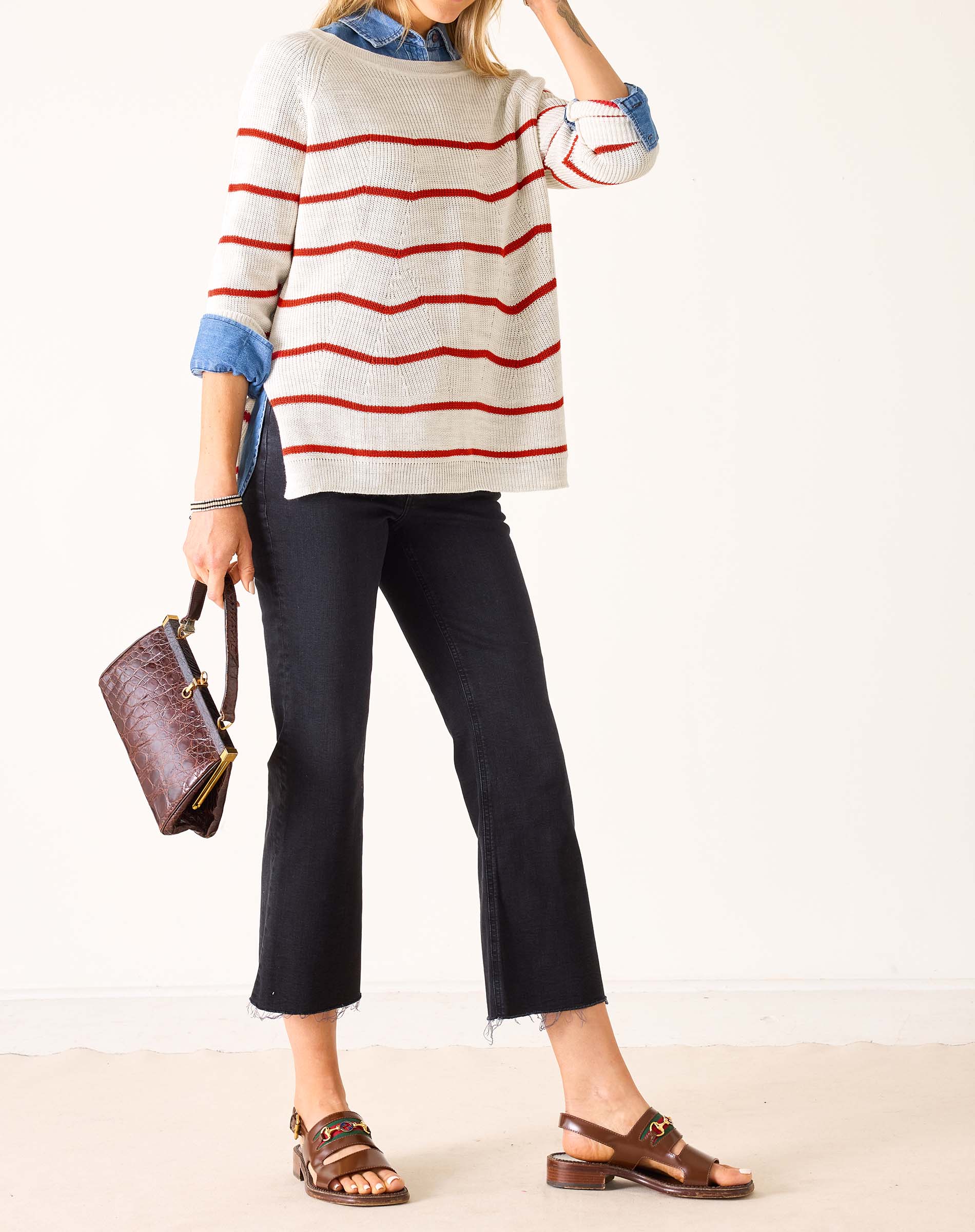Person wearing a striped sweater, black pants, and brown sandals on a white background