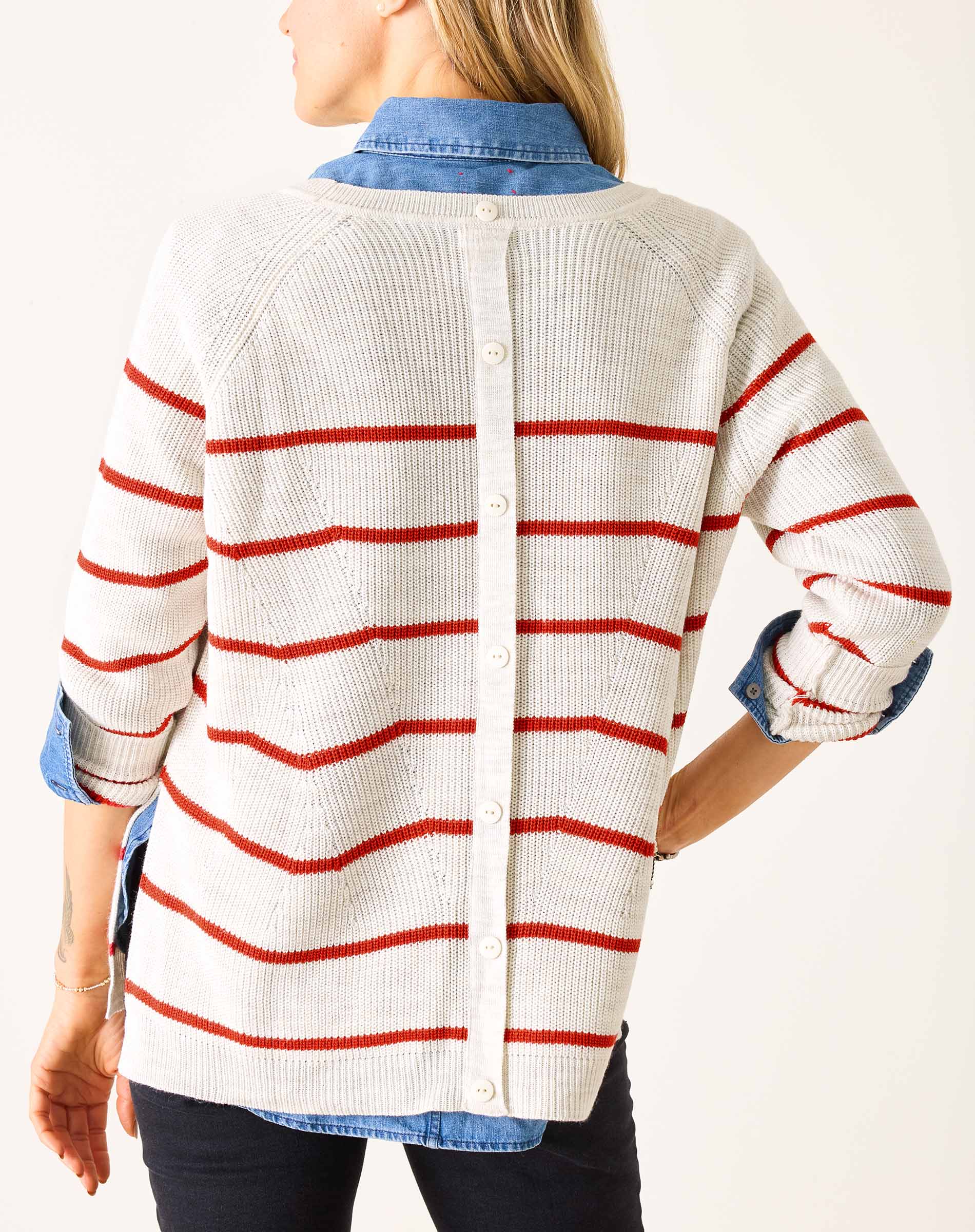 Person wearing a white cardigan with red stripes on a plain background