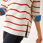 Person wearing a white sweater with red stripes and blue sleeves on a plain background