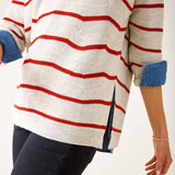 Person wearing a white sweater with red stripes and blue sleeves on a plain background