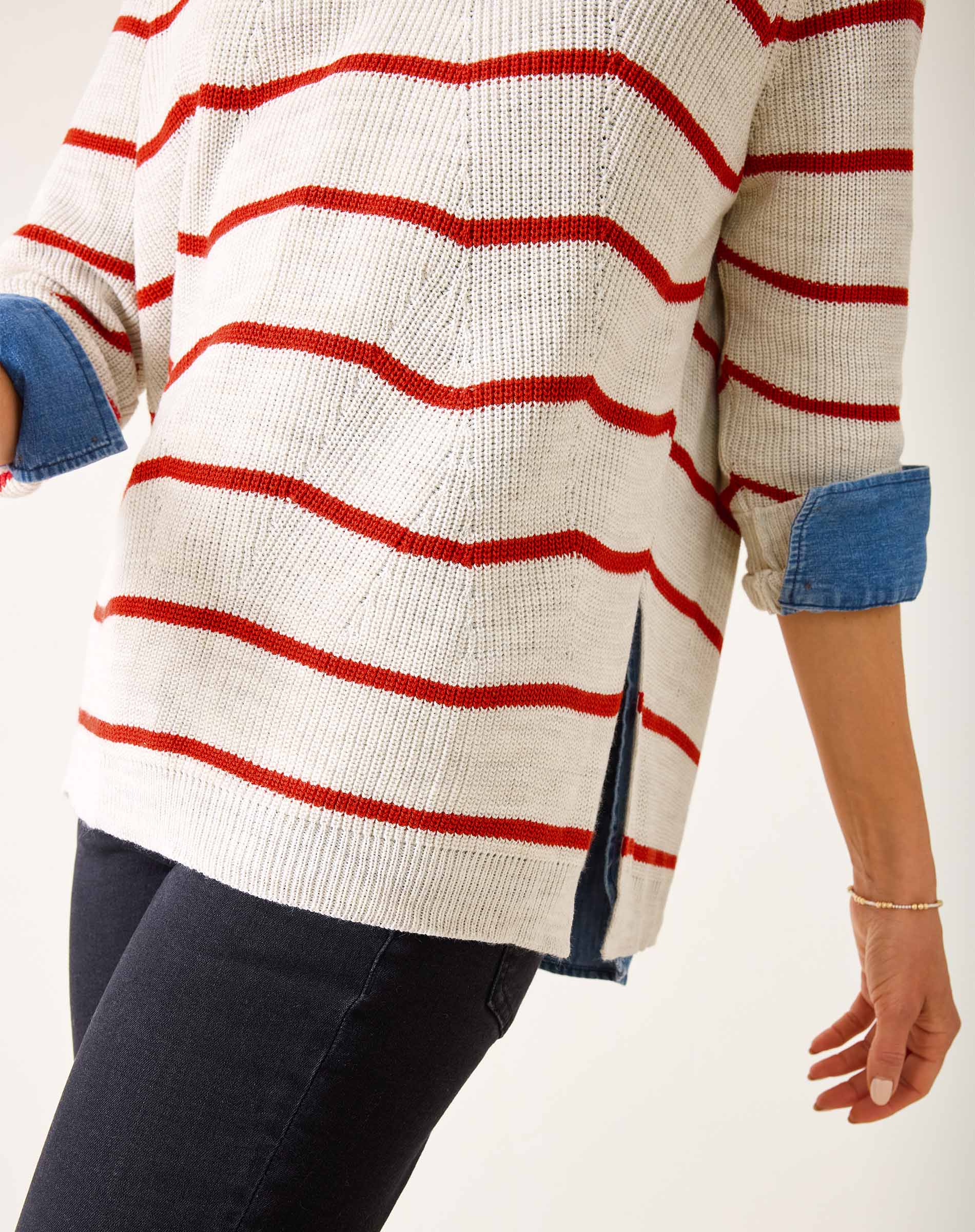 Person wearing a white sweater with red stripes and blue sleeves on a plain background