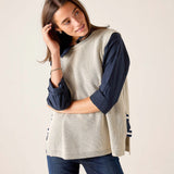 MERSEA ladies' travel-ready desert palm beige ribbed knit vest over a dark navy long-sleeve shirt and jeans.