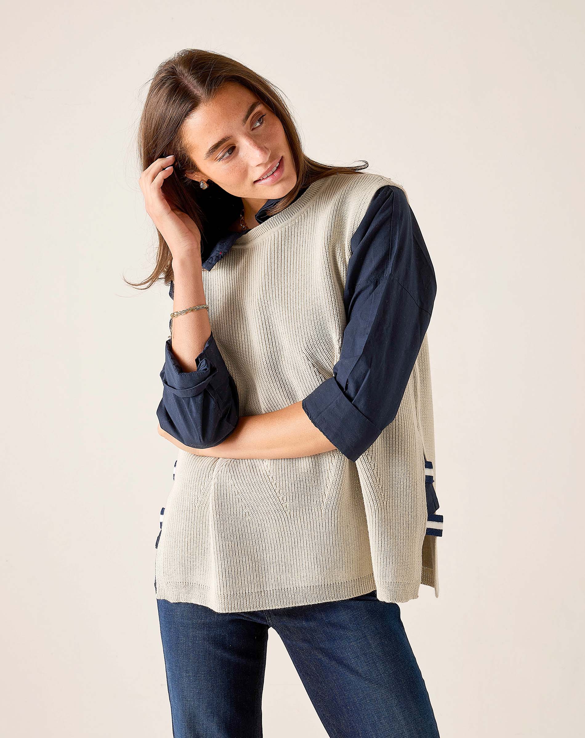 MERSEA ladies' travel-ready desert palm beige ribbed knit vest over a dark navy long-sleeve shirt and jeans.