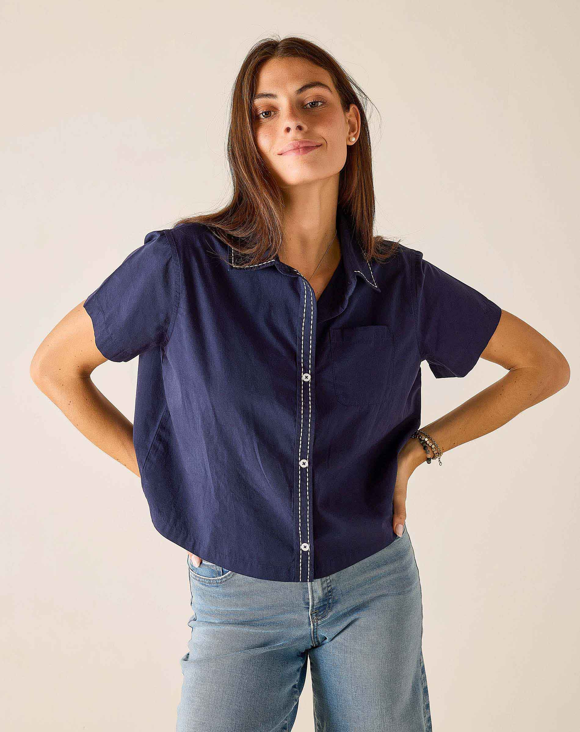 Woman wearing a navy blue shirt and light blue jeans against a plain background