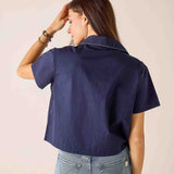 Person wearing a navy blue shirt and light blue jeans against a beige background
