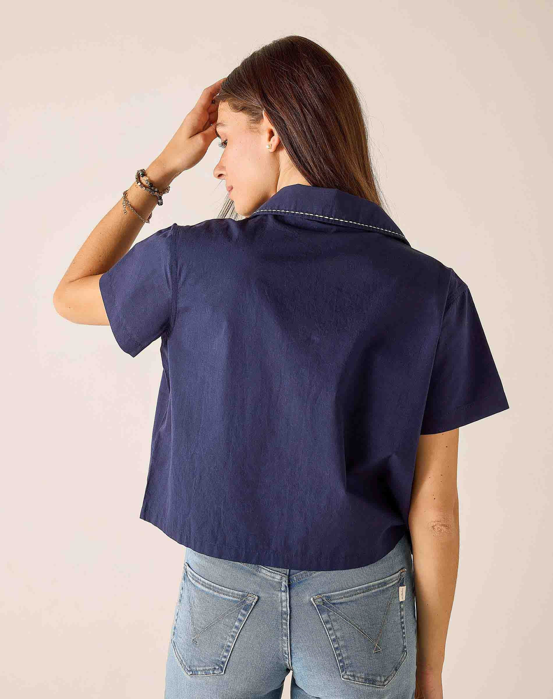 Person wearing a navy blue shirt and light blue jeans against a beige background