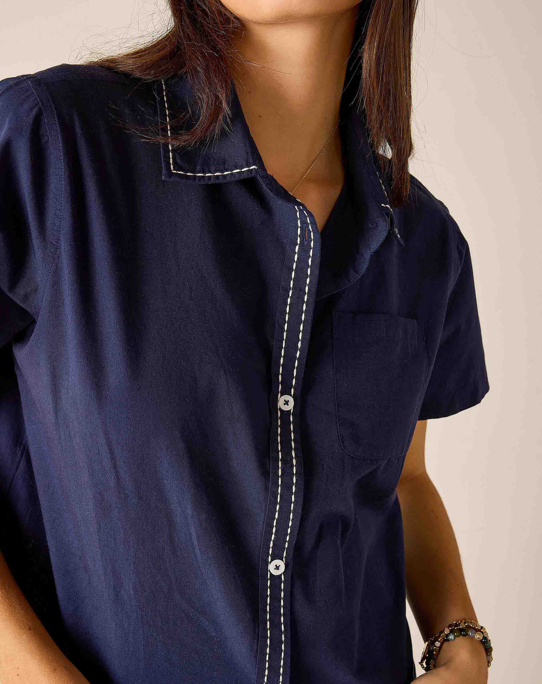 Navy blue shirt with white stitching worn by a person on a beige background