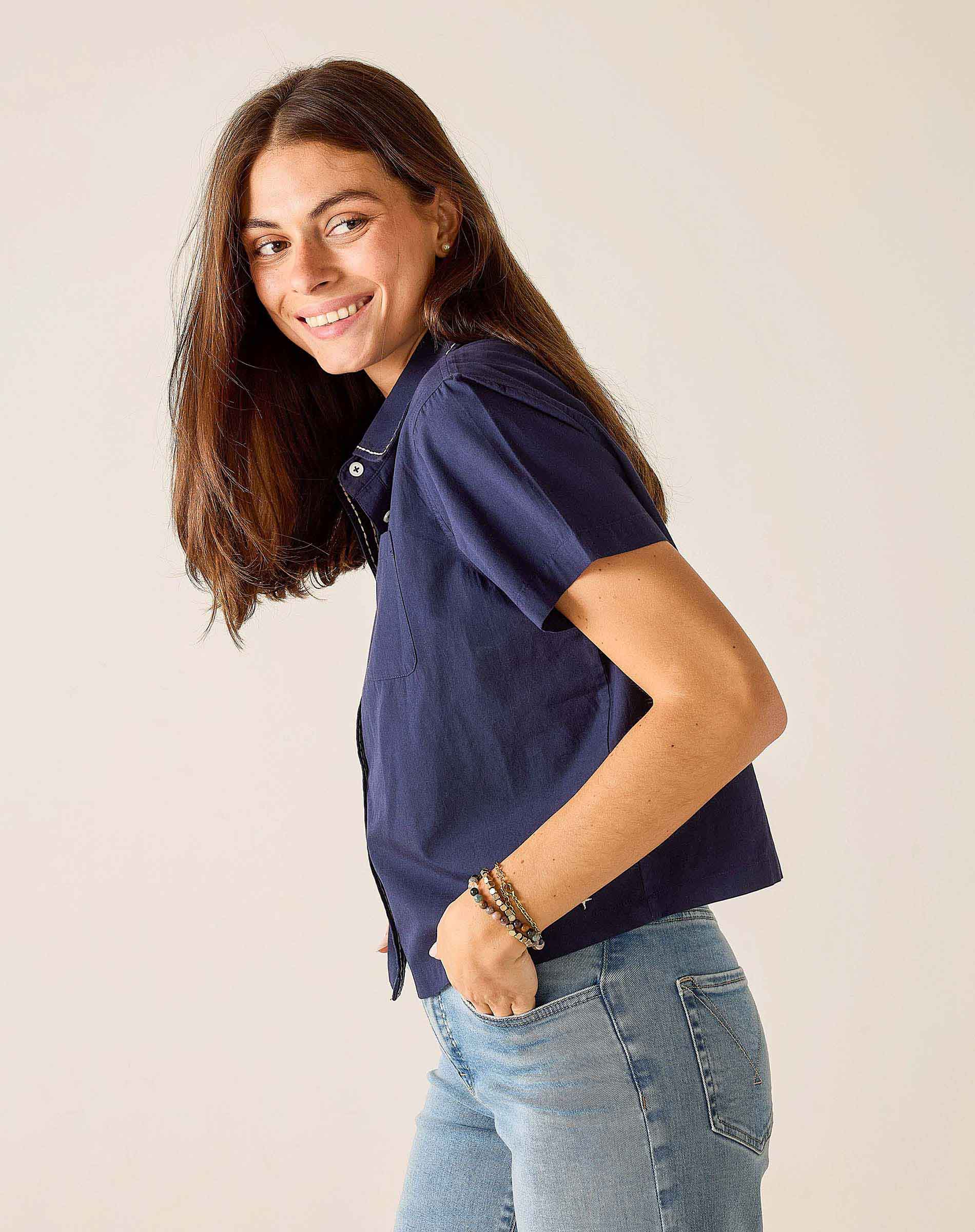 Woman wearing a navy blue shirt and light blue jeans against a plain background