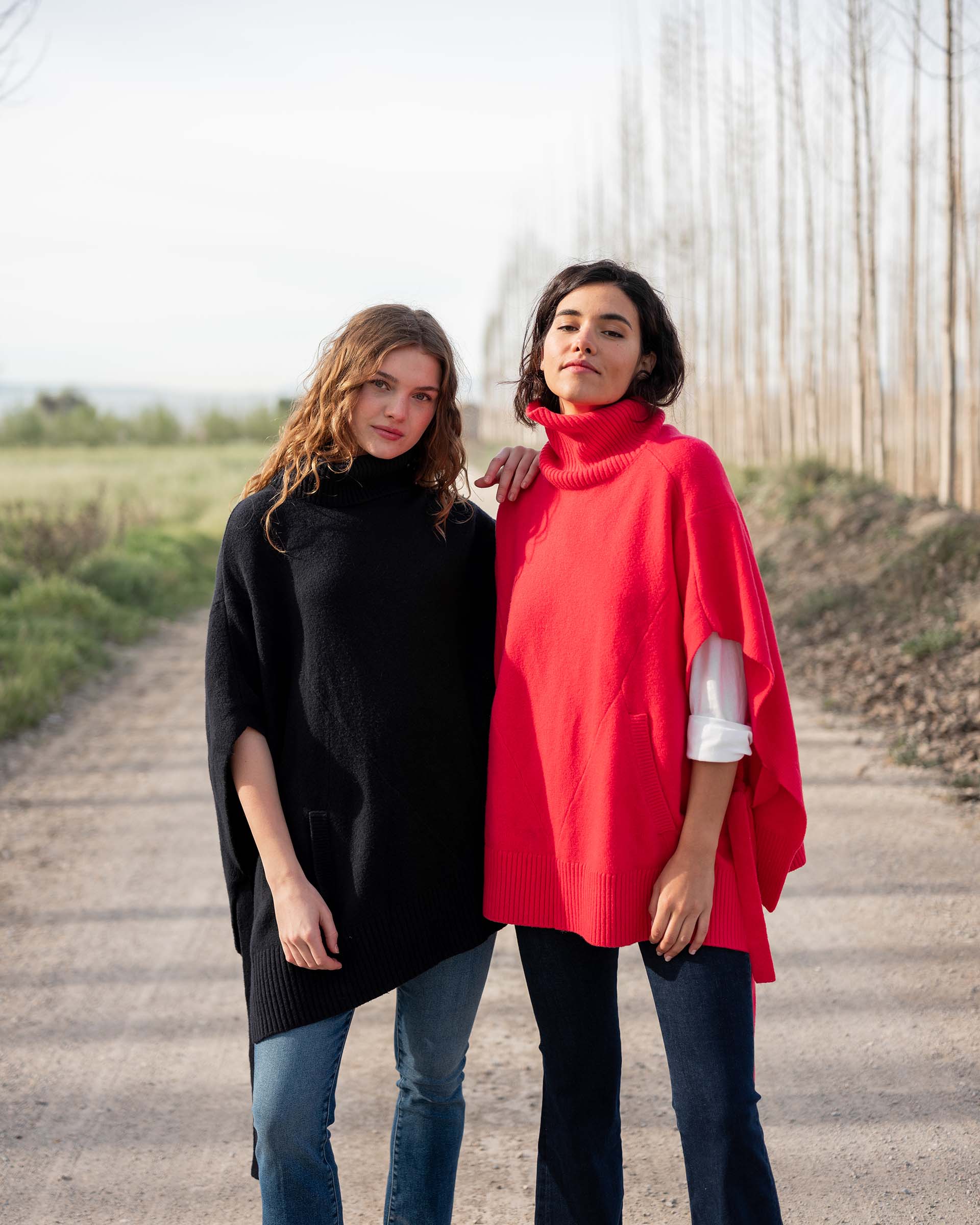 two women wearing mersea cape poncho sweaters in hibiscus red and navy blue
