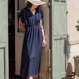 Woman in a navy dress and sun hat standing in front of a wooden door.