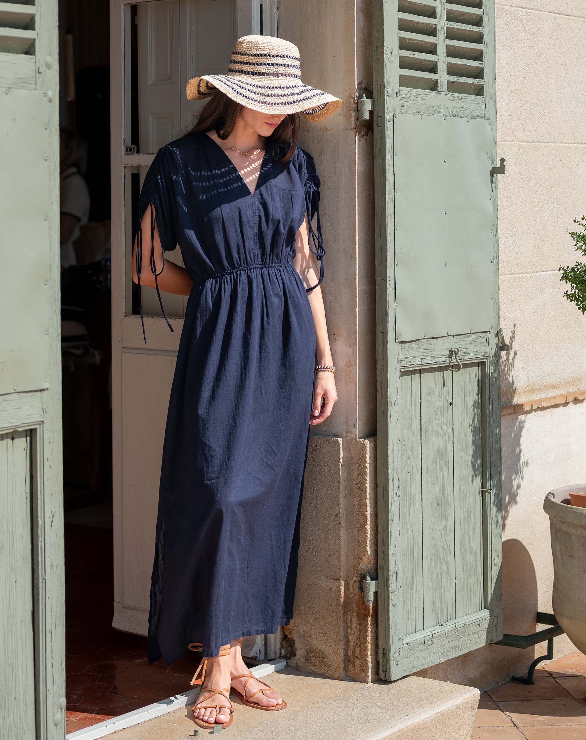 Woman in a navy dress and sun hat standing in front of a wooden door.