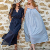 Two women in long dresses standing against a stone wall.