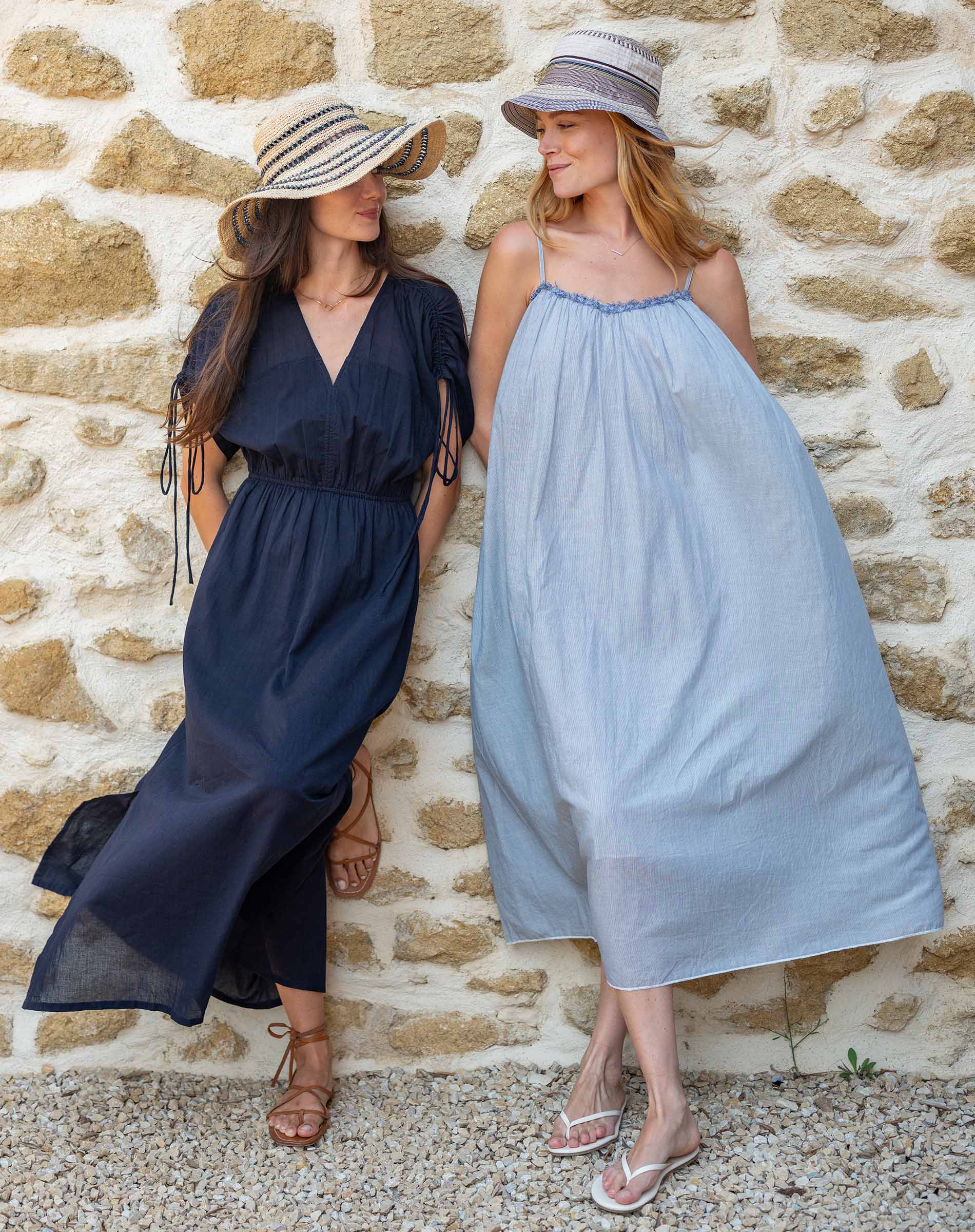 Two women in long dresses standing against a stone wall.