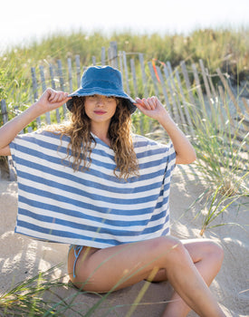 female wearing white and blue striped terry cloth slouch tee sitting on the beach in a swimsuit