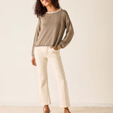 Woman wearing a beige sweater and white pants against a plain background
