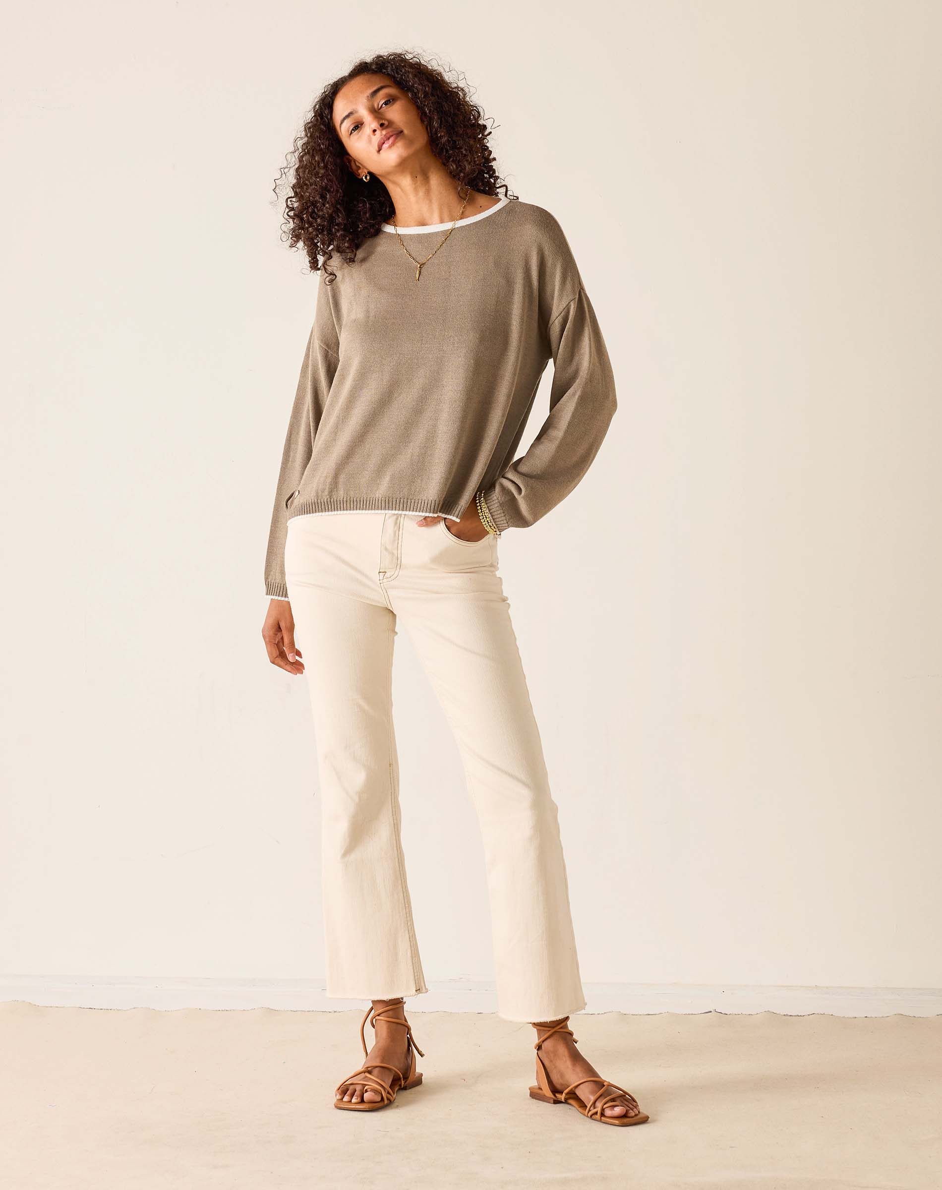 Woman wearing a beige sweater and white pants against a plain background