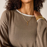 Woman wearing a brown sweater and gold jewelry against a neutral background