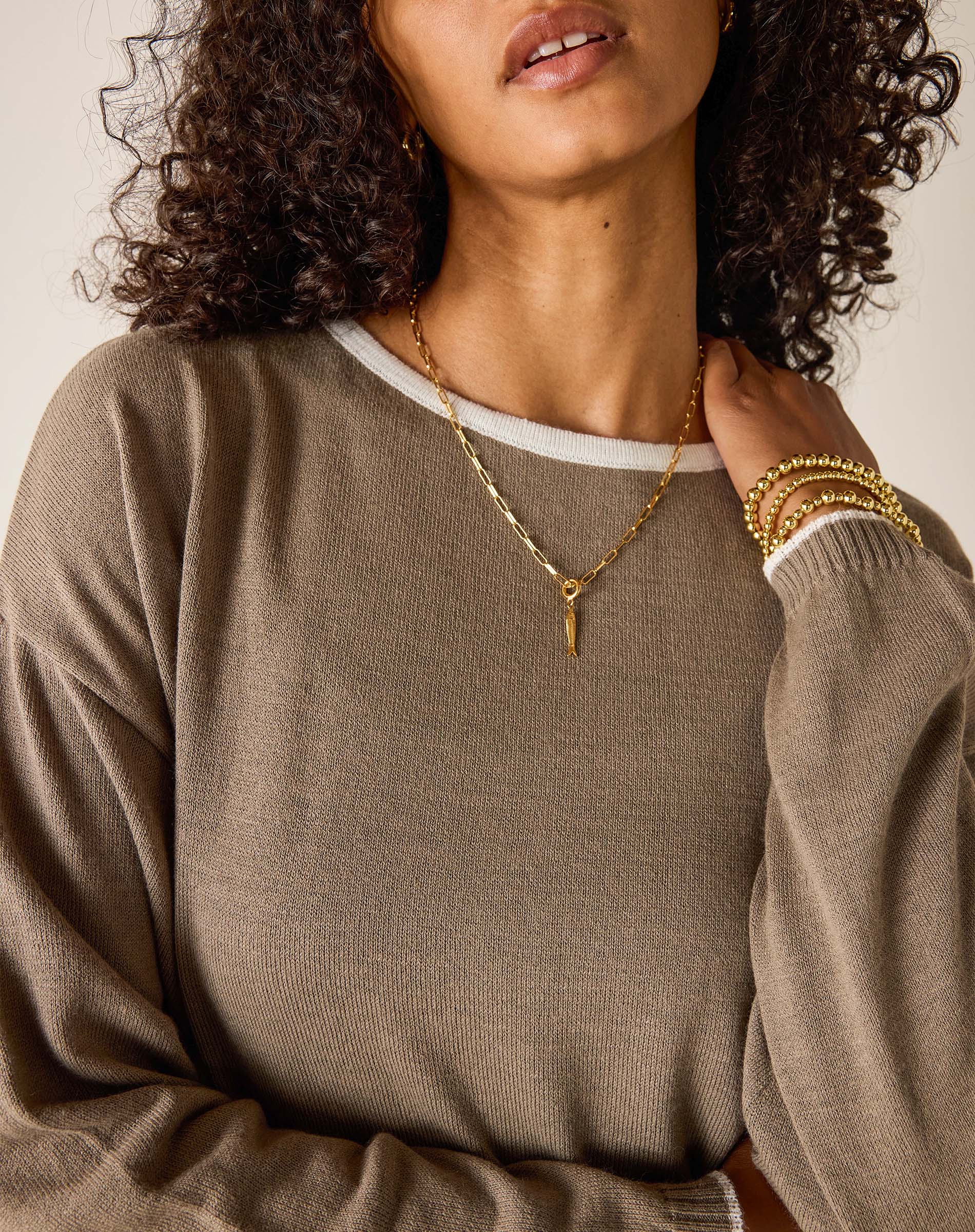 Woman wearing a brown sweater and gold jewelry against a neutral background