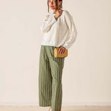 Woman wearing a white blouse and green striped pants, holding a wooden clutch against a plain background