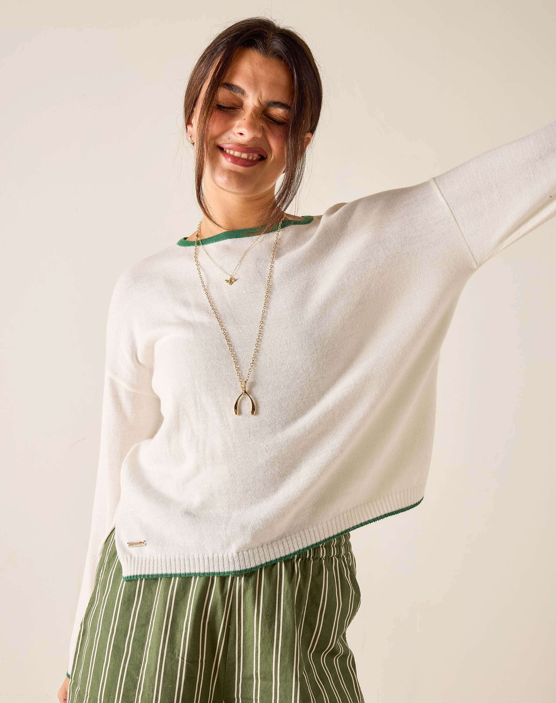 Woman wearing a white sweater with green trim and striped pants, standing against a plain background.