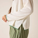 Person wearing a white sweater with green trim and green striped pants on a plain background