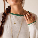 Woman wearing a gold necklace with a green trim on a neutral background