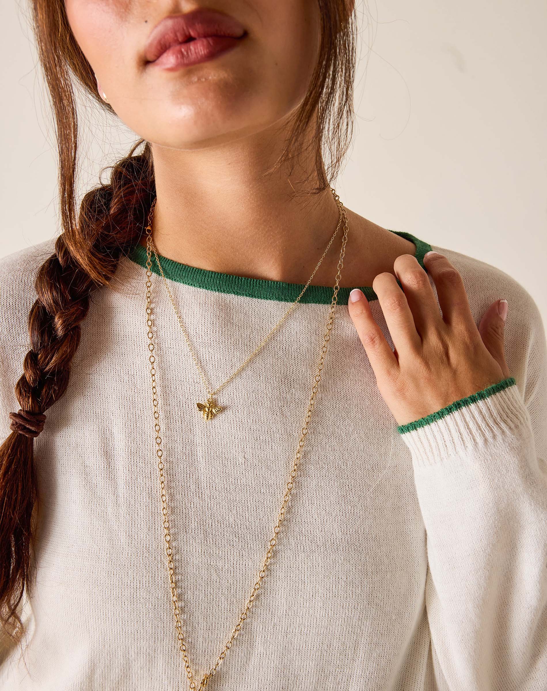 Woman wearing a gold necklace with a green trim on a neutral background