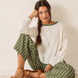 Woman wearing a white sweater and green striped pants sitting on a light-colored floor.