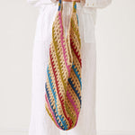 Colorful crocheted bag held by a person wearing a white outfit on a plain background