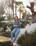 woman wearing mersea carmel cashmere sweater in indigo sitting outside against wall